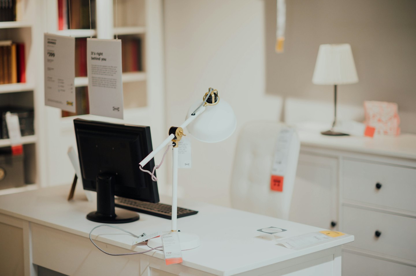 Modern white desk with computer and lamp.