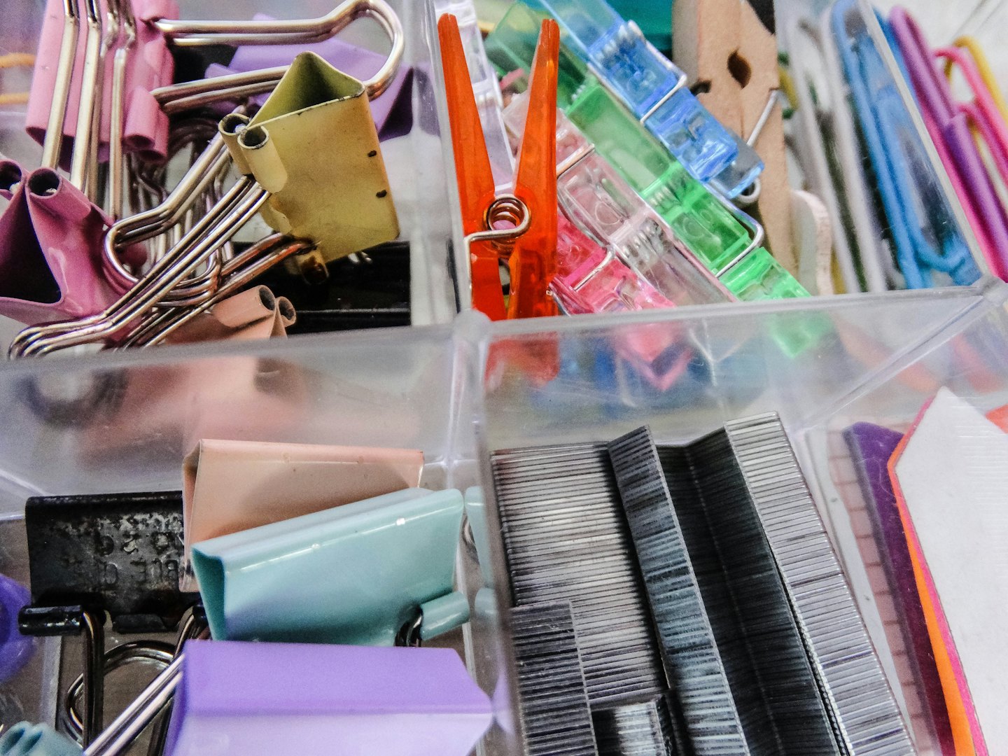 Desk organizer filled with colorful binder clips, mini clothespins, and staples.