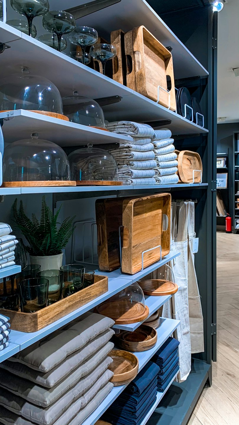 Shelves display kitchenware, cushions, and textiles in a retail store.